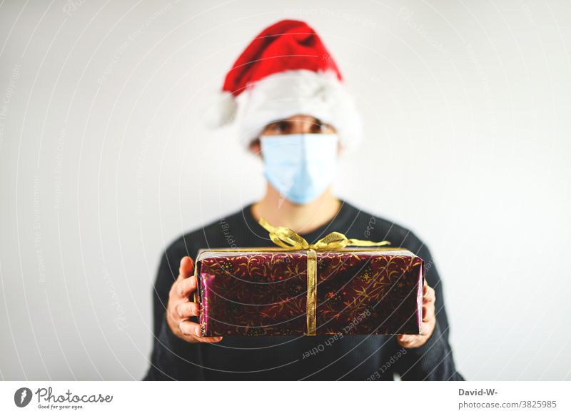 merry christmas - man holds gift in his hands under corona conditions Christmas Gift Respirator mask Mask Santa Claus hat Giving of gifts pandemic Protection