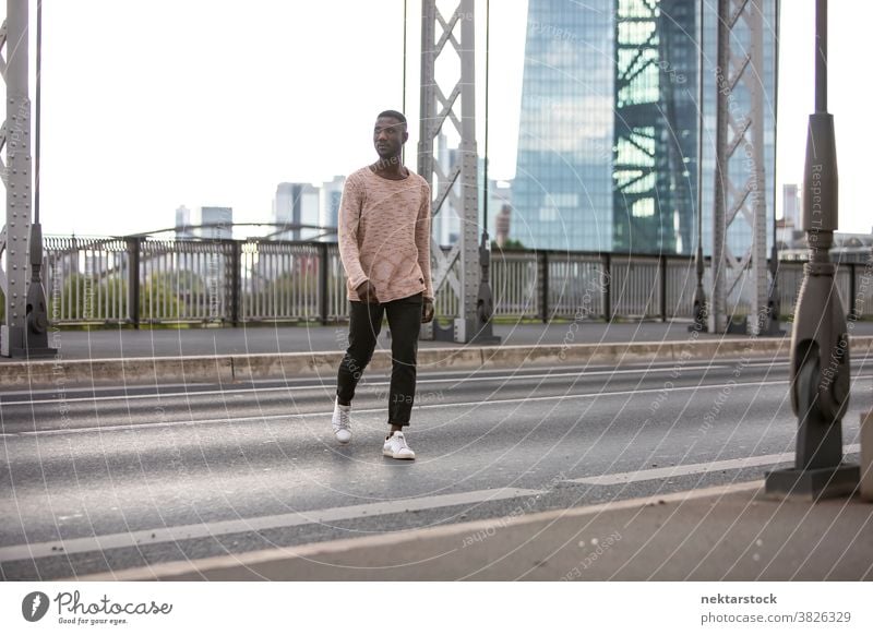 Man Crossing Street with Head Turned man street cross walking crossing sweater looking away head turned front view African ethnicity city life long shot