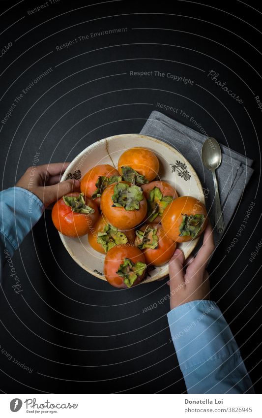 Plat of persimmon and hands autumn biologic black background copy space dark delicious food fruits good healthy holding indoor many nutrition orange plat spoon