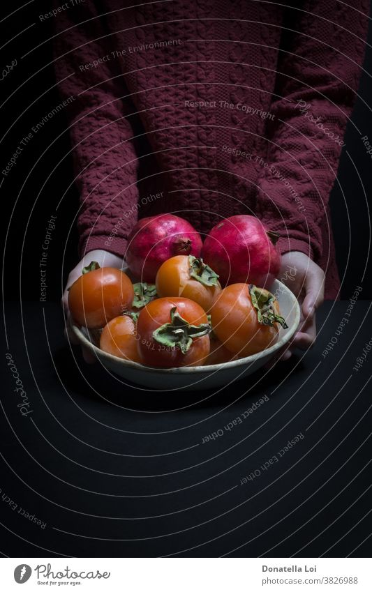 Plat of persimmon and pomegranates autumn biologic black background copy space dark delicious food fruits good hands healthy holding indoor many nutrition