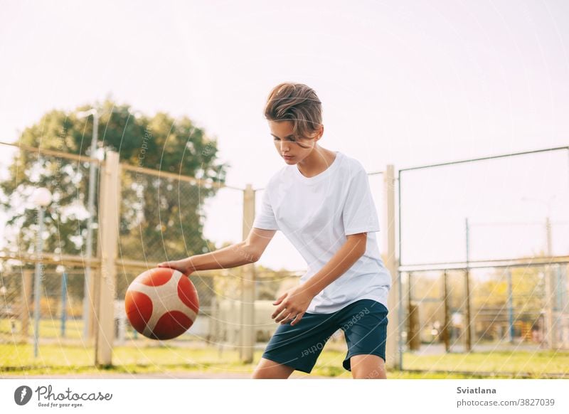 Focused cute boy athlete leads the ball in a game of basketball. A boy plays basketball after school. Sports, healthy lifestyle, leisure dribbling sport player