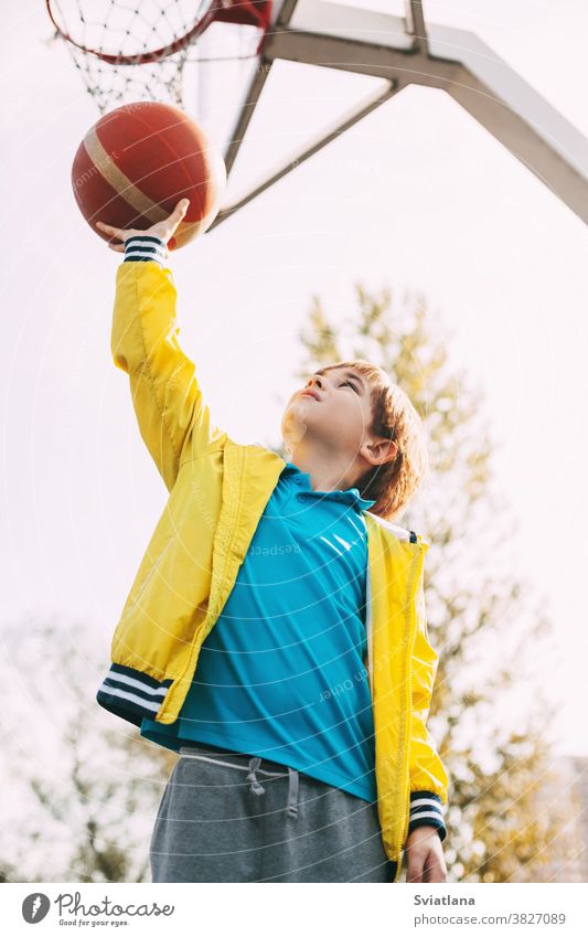 Portrait of a cute boy basketball player standing with a ball in his hands next to the basketball Hoop. The concept of sport and a healthy lifestyle game active