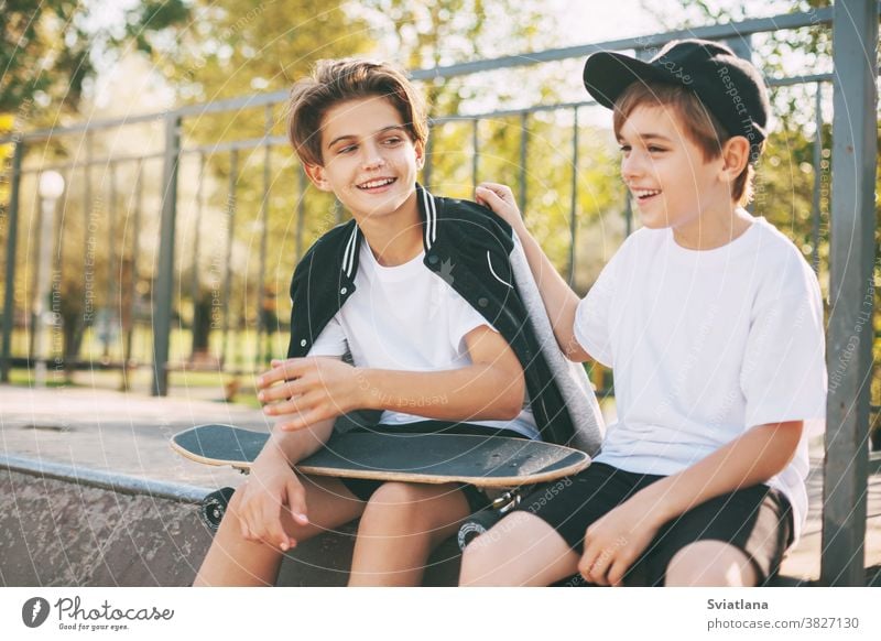 Two cute teenagers sit in a skatepark, relax after skateboarding and chat. Boys enjoy their free time in the skate Park, sitting on the ramp. The concept of youth, unity and friendship