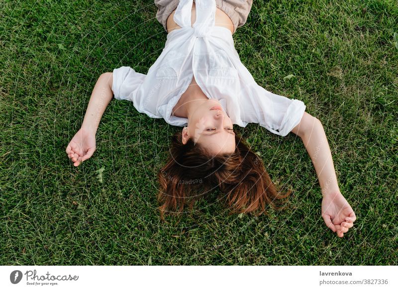 Above shot of woman lying on green grass girl female lifestyle adult person outdoors park happy top view above faceless hands summer seasonal relaxed peaceful