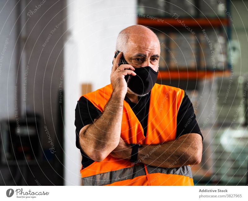 Concentrated male warehouse worker talking on smartphone man conversation phone call serious manager at work workplace protect occupation mask storehouse