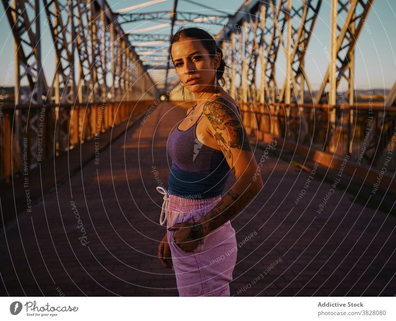 Stylish woman in tattoos standing in city style trendy bridge metal sunset summer relax rest enjoy young urban freedom delight glad evening twilight cool