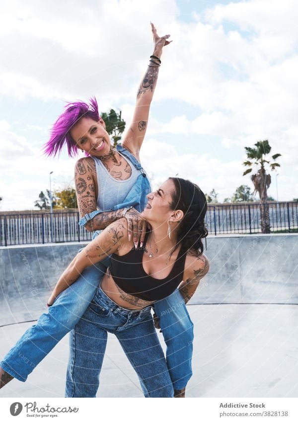 Cheerful women having fun together in skate park piggyback friend friendship informal tattoo subculture cool delight laugh optimist weekend happy joy carefree