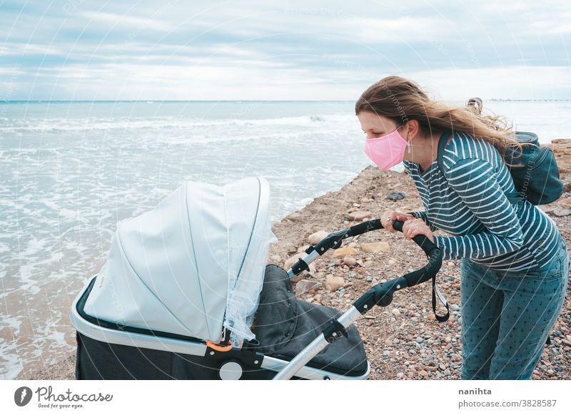 Young mom walking with her baby during covid pandemic covid-19 coronavirus motherhood family holidays mask face mask daughter beach outdoors sea shore autumn