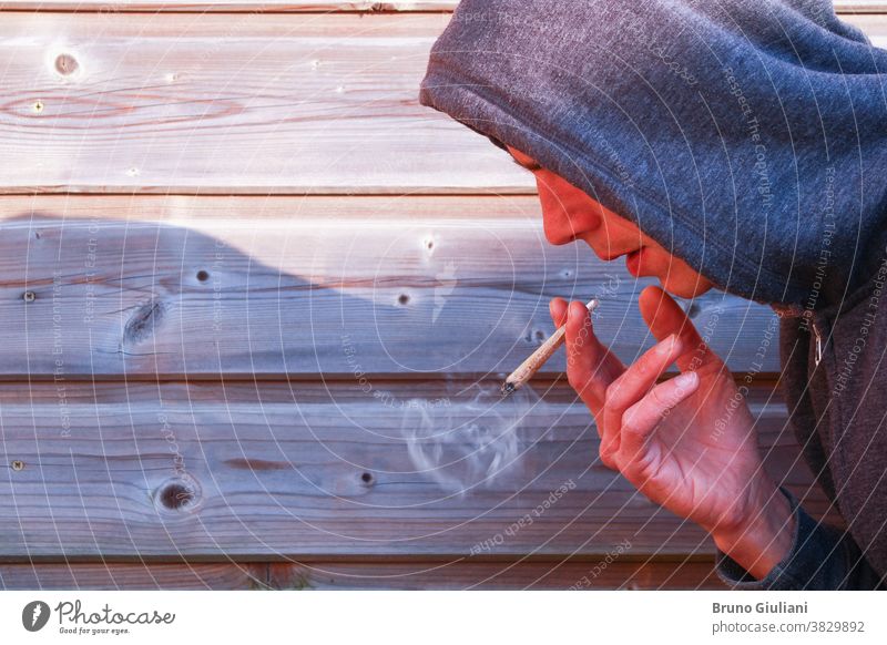 Boy with a rolled cigarette with a wrinkled hand. Man alone smoking marijuana against a wooden picket fence. drug joint portrait cannabis addiction adult weed