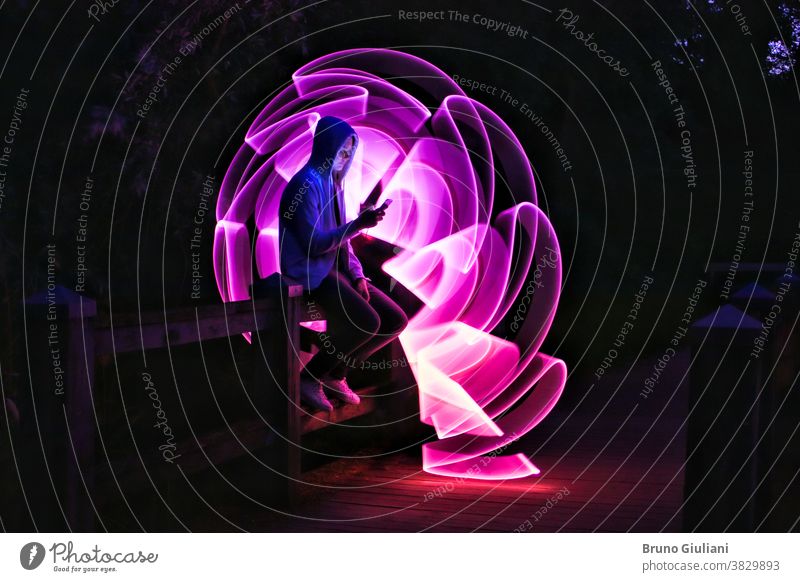Man sitting on a bridge with his smartphone in his hand. People using technology. Purple abstract shape with a bright sword in the background. Lightpainting scene.