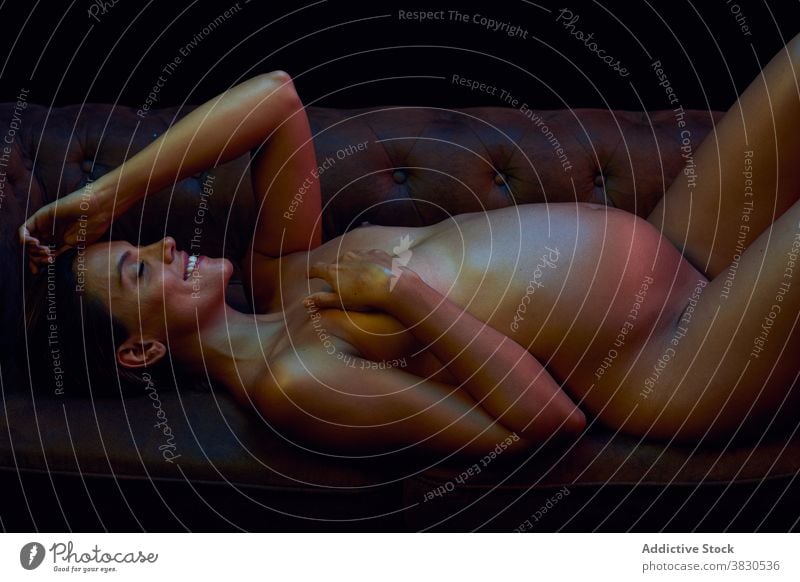 Sensual pregnant woman lying on sofa in darkness belly erotic motherhood smiling anticipate expect hot sexy naked female smile tummy nude parenthood fertile
