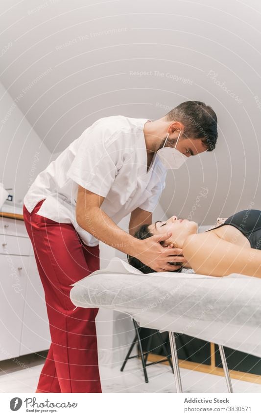 Male therapist doing procedures with client in clinic physiotherapy treat doctor patient table medical health care professional neck gown mask healthy