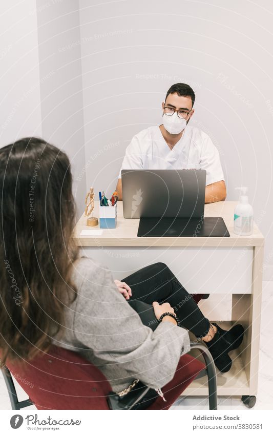Serious doctor with patient in medical room in hospital man work laptop mask clinic typing physician male busy occupation specialist device using table gadget