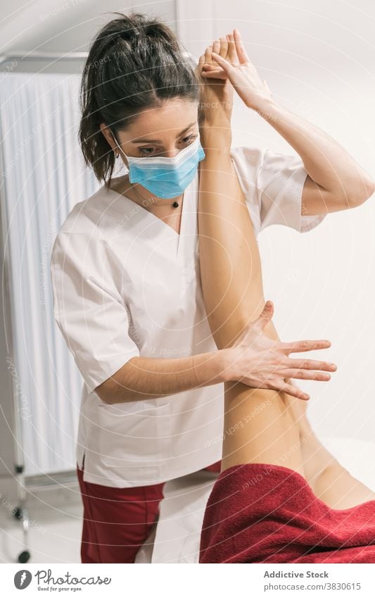 Physiotherapist stretching leg of patient in medical room rehabilitation physiotherapy help treat mask health care professional doctor procedure contemporary