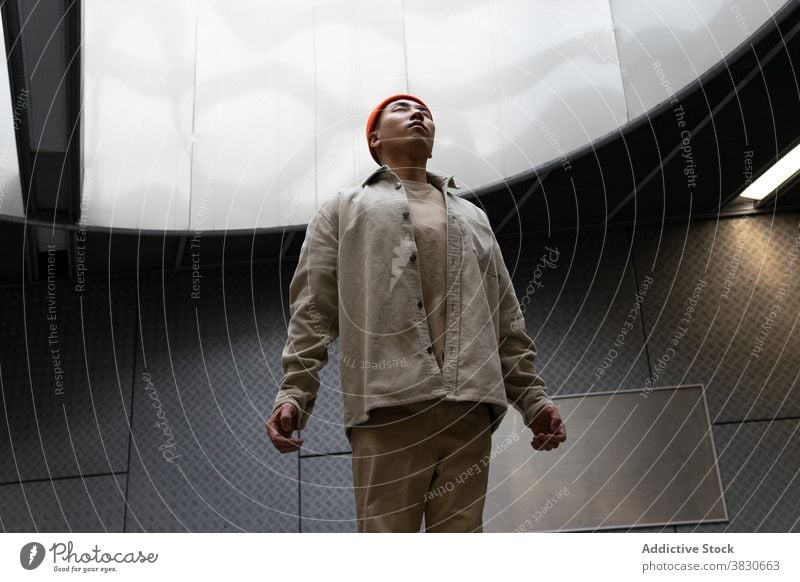 Calm Asian man levitating above floor in corridor above ground levitate calm hover serious hallway focus concentrate thoughtful pensive ponder gray positive