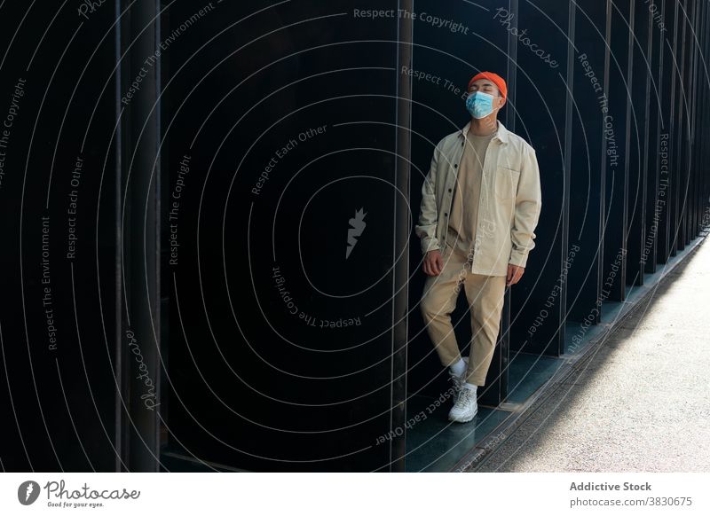 Emotionless Asian man in face mask leaning on building wall unemotional melancholy cover mouth pandemic coronavirus thoughtful lean on eyes closed facade