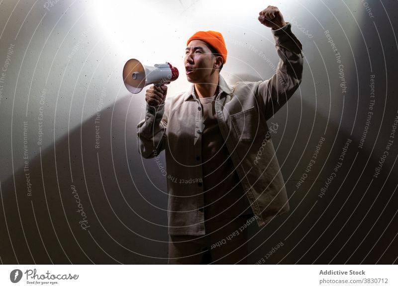 Expressive man shouting in megaphone against gray wall scream overwhelmed expressive loudspeaker darkness emotion exclaim voice yell call confident modern
