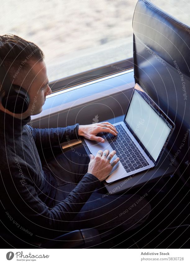 Man in headphones working on laptop in train business trip man freelance remote typing travel male seat modern passenger gadget device young netbook guy journey