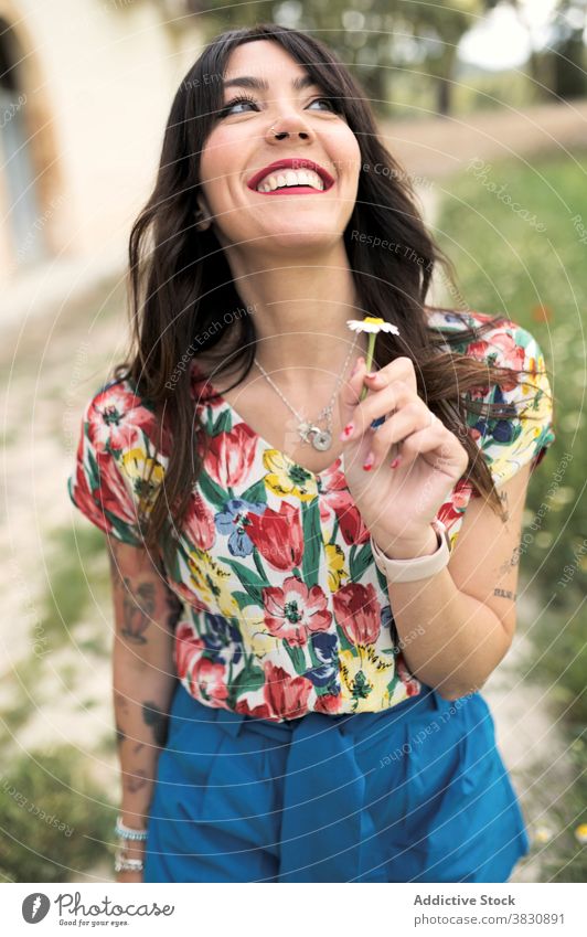 Cheerful woman with chamomile in hand on street toothy smile charming cheerful flower happy summer pretty outfit style female plant daisy delight enjoy