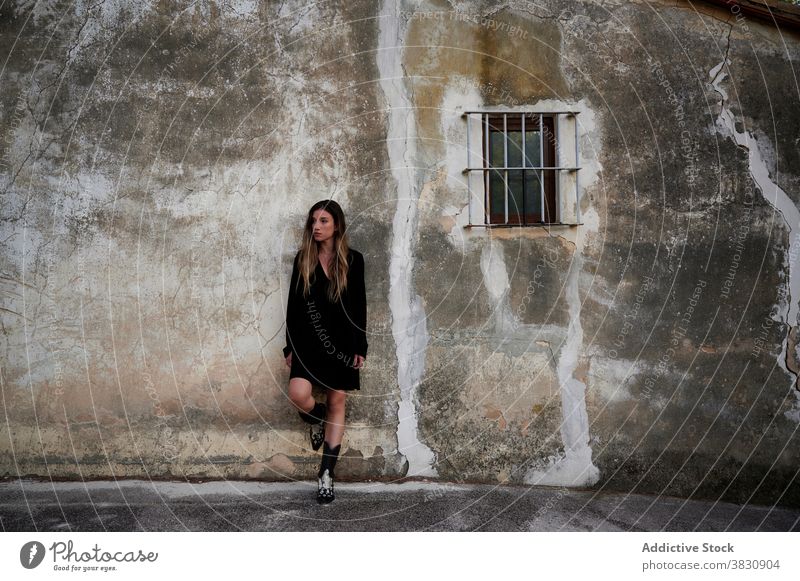 Woman in black dress standing near weathered building woman shabby wall aged grunge alone gloomy depression young female exterior ancient house calm tranquil