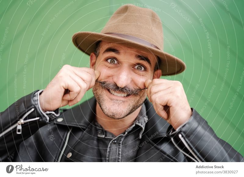 Happy man with mustache in hat grimacing curl make face fun cheerful grimace leather jacket male glad smile pretend metrosexual optimist positive joy confident