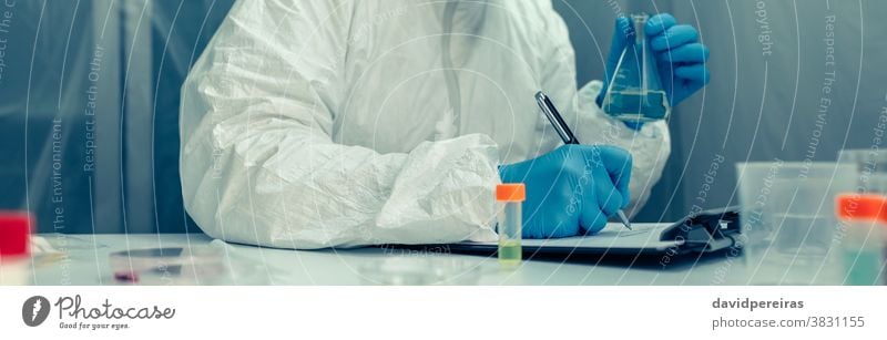 Scientist with protection suit investigating in the laboratory scientist bacteriological protection suit test tube virus coronavirus taking notes vaccine