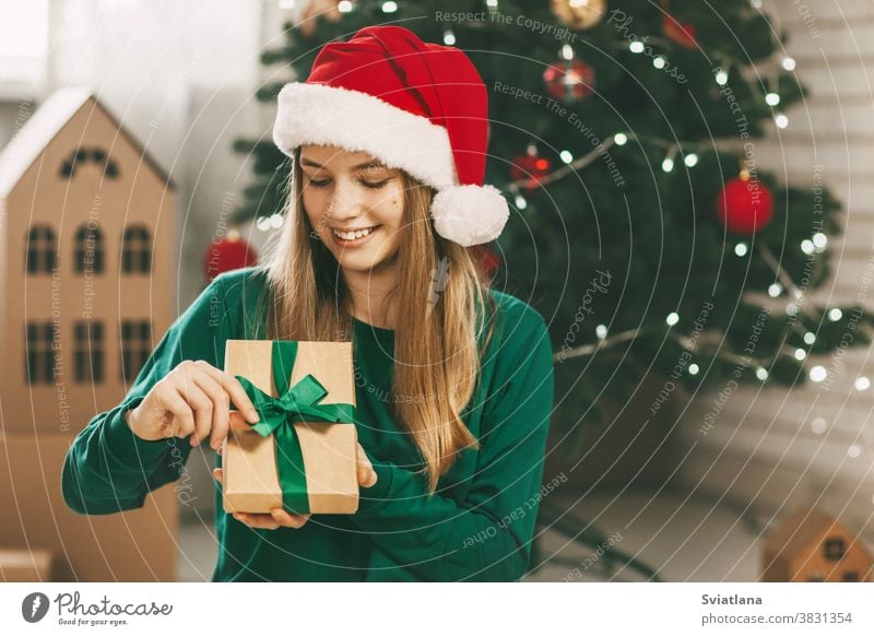 Beautiful teenage girl opens a gift made of kraft paper tied with a green ribbon, new year mood. Holiday concept of Christmas and New Year at home. christmas