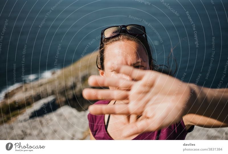 Playful woman trying to hide from photographer camera to avoid pics. mountain sea nature coast outdoors arm hand timid shame joyful playful shy expressive cover