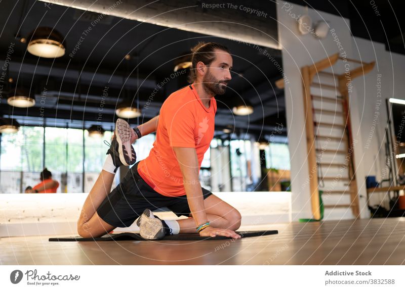 Bearded sportsman stretching in gym training fitness flexible modern floor healthy male athlete adult strong strength endurance effort workout exercise wellness
