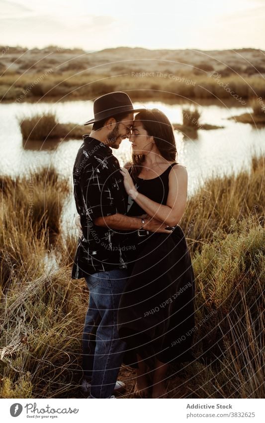 Dreamy couple on coast of pond at sunset love field affection relationship romantic meadow woman boyfriend girlfriend nature affair together hug embrace touch