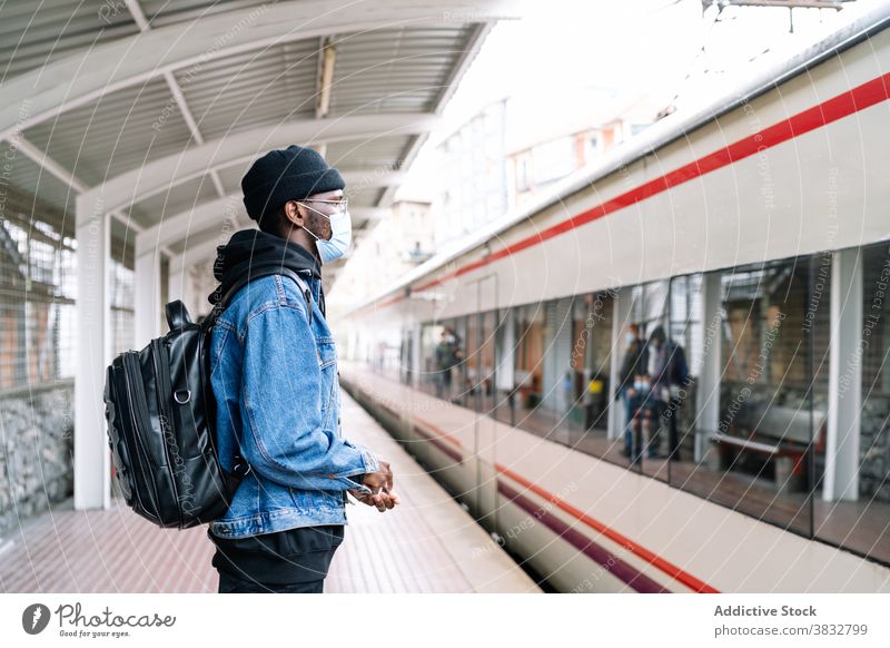 Black man on platform with train railway traveler mask coronavirus new normal tourist station male ethnic black african american backpack urban trip journey