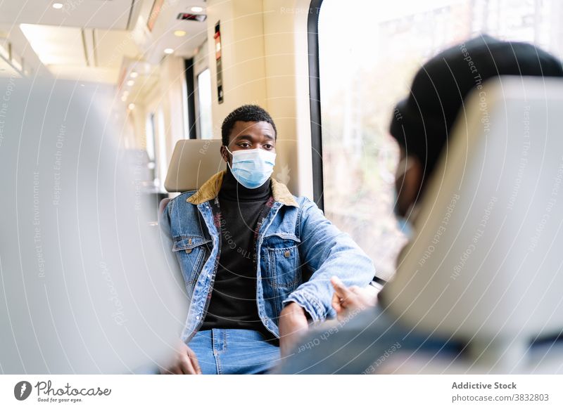 Male friends riding in train during coronavirus pandemic ride passenger men travel new normal window mask railroad ethnic black african american medical trip