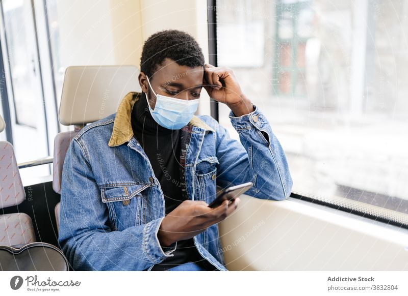 Traveling black man using cellphone in train passenger smartphone new normal travel mask coronavirus railroad railway male ethnic african american tourist