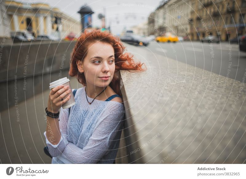 Young woman with takeaway coffee resting on city street relax thoughtful drink redhead positive dreamy millennial female cup saint petersburg russia