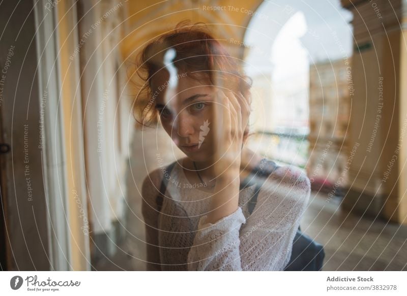 Young woman looking through window of old building curious redhead urban pensive travel reflection lonely young female russia saint petersburg explore peek peep