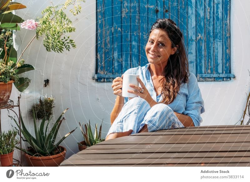 Smiling woman drinking coffee on terrace happy cheerful rest cup adult ethnic female beverage optimist glad smile relax lifestyle break enjoy content mug