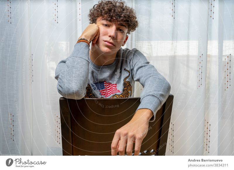 Attractive young man with curly hair wearing gray sweatshirt posing on white curtains background cheerful casual smile male adult handsome happy attractive