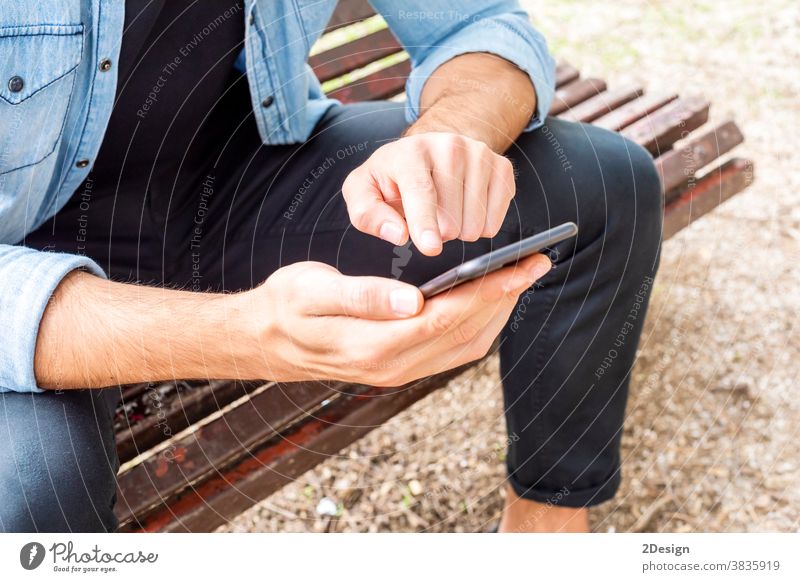 Closeup up an Attractive young man sitting on a bench outside using his cell phone outdoors holding mobile phone smiling urban male person lifestyle city