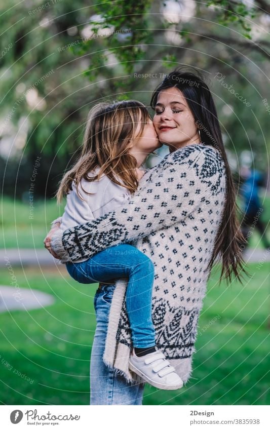 Little cute child baby girl kiss on cheek and hug, embrace with happy pretty woman in green park. Mother, little kid daughter. Mother's Day, love family, parenthood, childhood