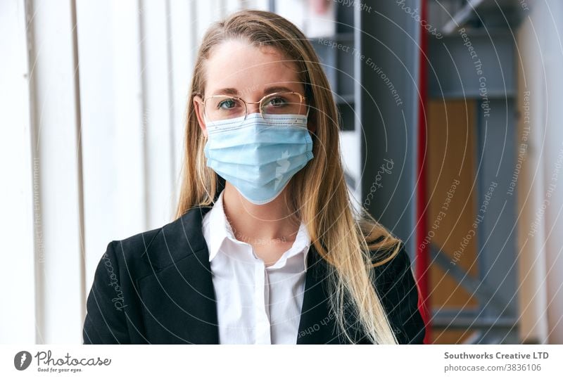 Portrait Of Young Businesswoman Wearing Mask Standing In Modern Office During Health Pandemic business businesswoman face mask face covering wearing ppe working