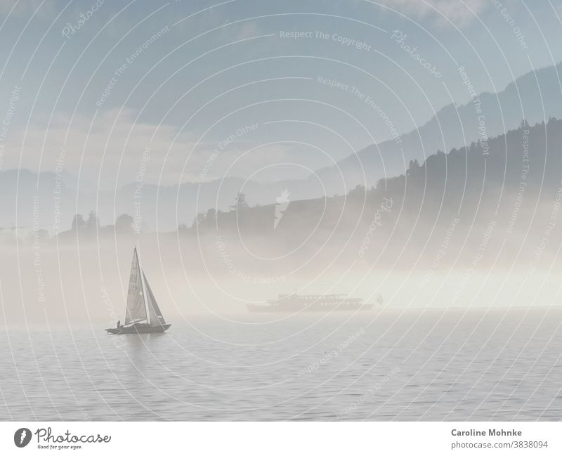 A rare fog atmosphere on Lake Lucerne: a sailing ship in the foreground, a blanket of fog on the lake in the background. Another ship can be seen in it and in the background the Alps.