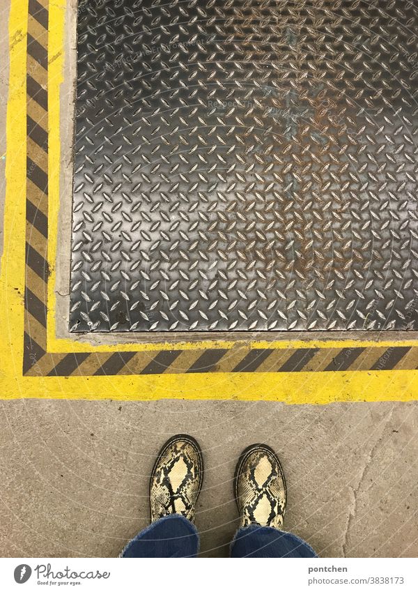 Pattern mix. Snakeskin shoes in front of striped floor marking and manhole cover Manhole cover Footwear Stripe Covers (Construction) Shaft Protection iron cover