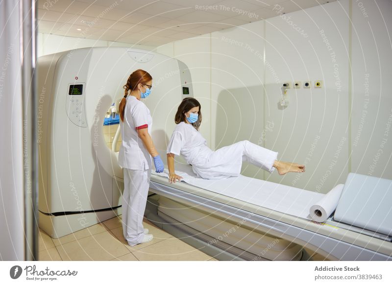 Radiologist and patient on tomography equipment in clinic radiologist diagnostic health care uniform mask professional women together lying couch scan machine
