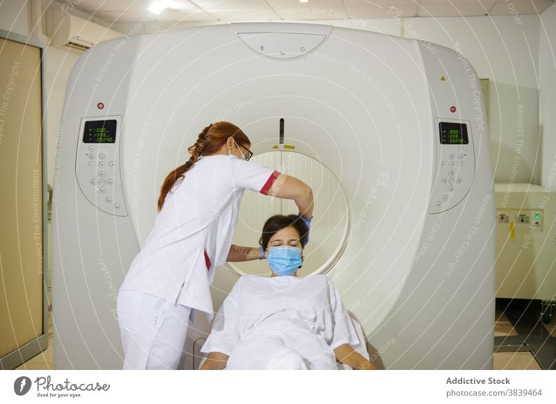 Unrecognizable radiologist and patient on tomography equipment in clinic diagnostic health care uniform mask professional women together lying couch scan