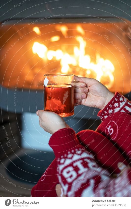 Crop woman with cup of tea near fireplace christmas cozy warm atmosphere chimney holiday night female red xmas new year sweater relax beverage winter drink sit