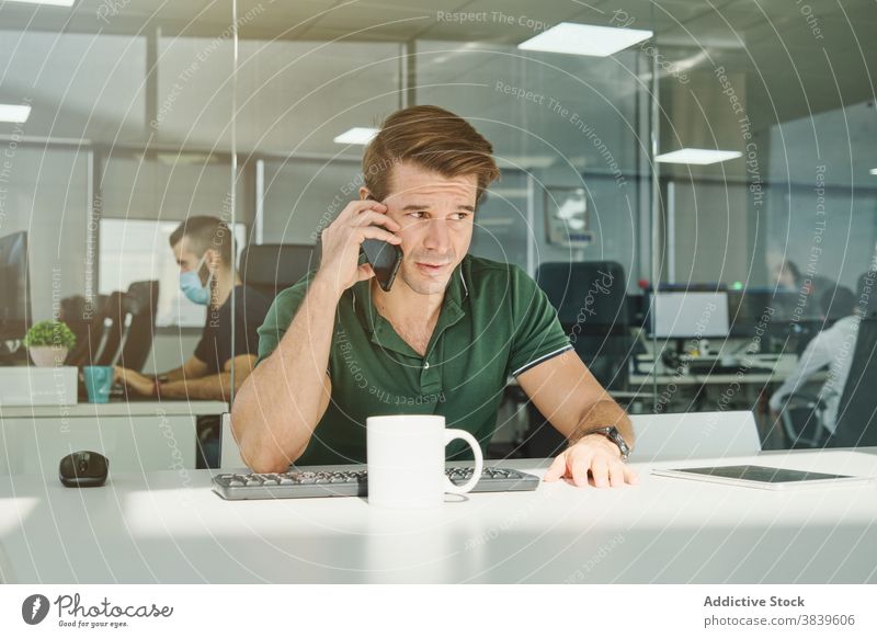 Male office worker talking on smartphone at table man discuss project smile workplace employee male cellphone busy business professional conversation modern sit