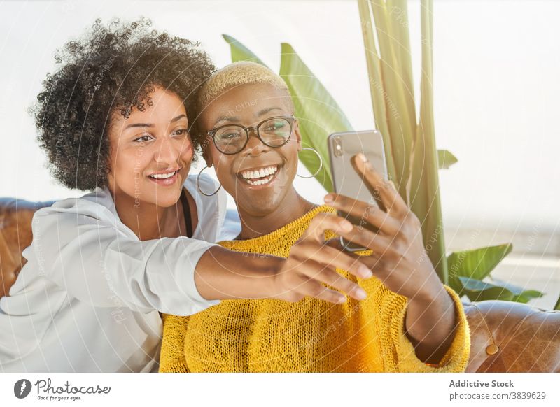 Delighted black lesbian couple taking selfie on smartphone women love lgbt self portrait hug equal ethnic african american mobile smile armchair embrace device