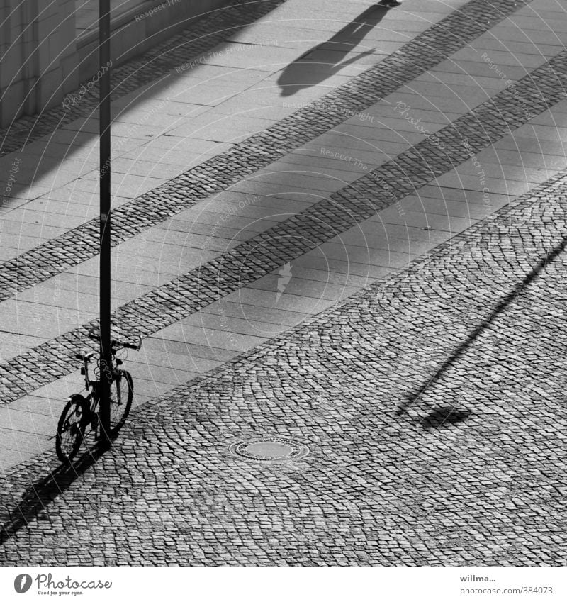 A bicycle stands, a person comes, and the shadow of a street lamp pushes its way into the picture. Bicycle Shadow Human being Places Lamp post Shadow play B/W
