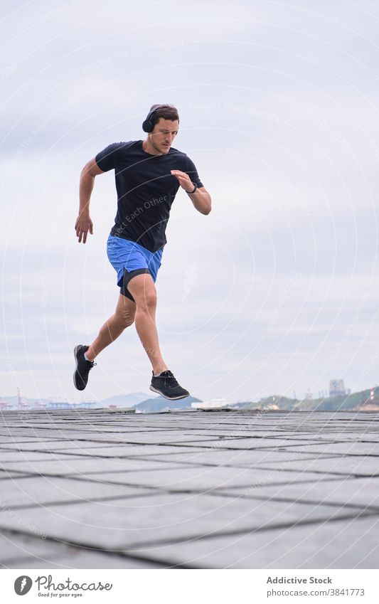 Sportive man jumping during training in city sportsman runner workout active determine dynamic male cardio cloudy healthy energy urban sportswear endurance