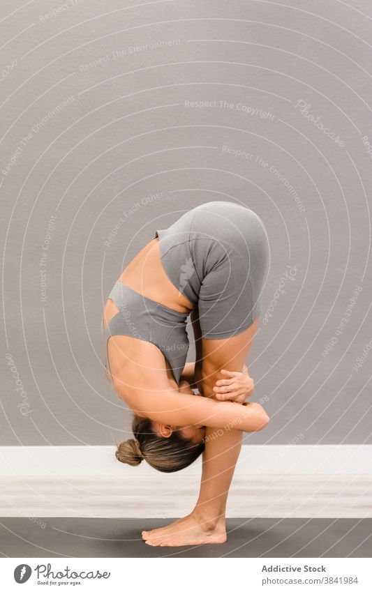 Flexible woman standing in forward bend on yoga mat asana stretch flexible uttanasana practice barefoot female sportswear fit slim peaceful balance posture pose